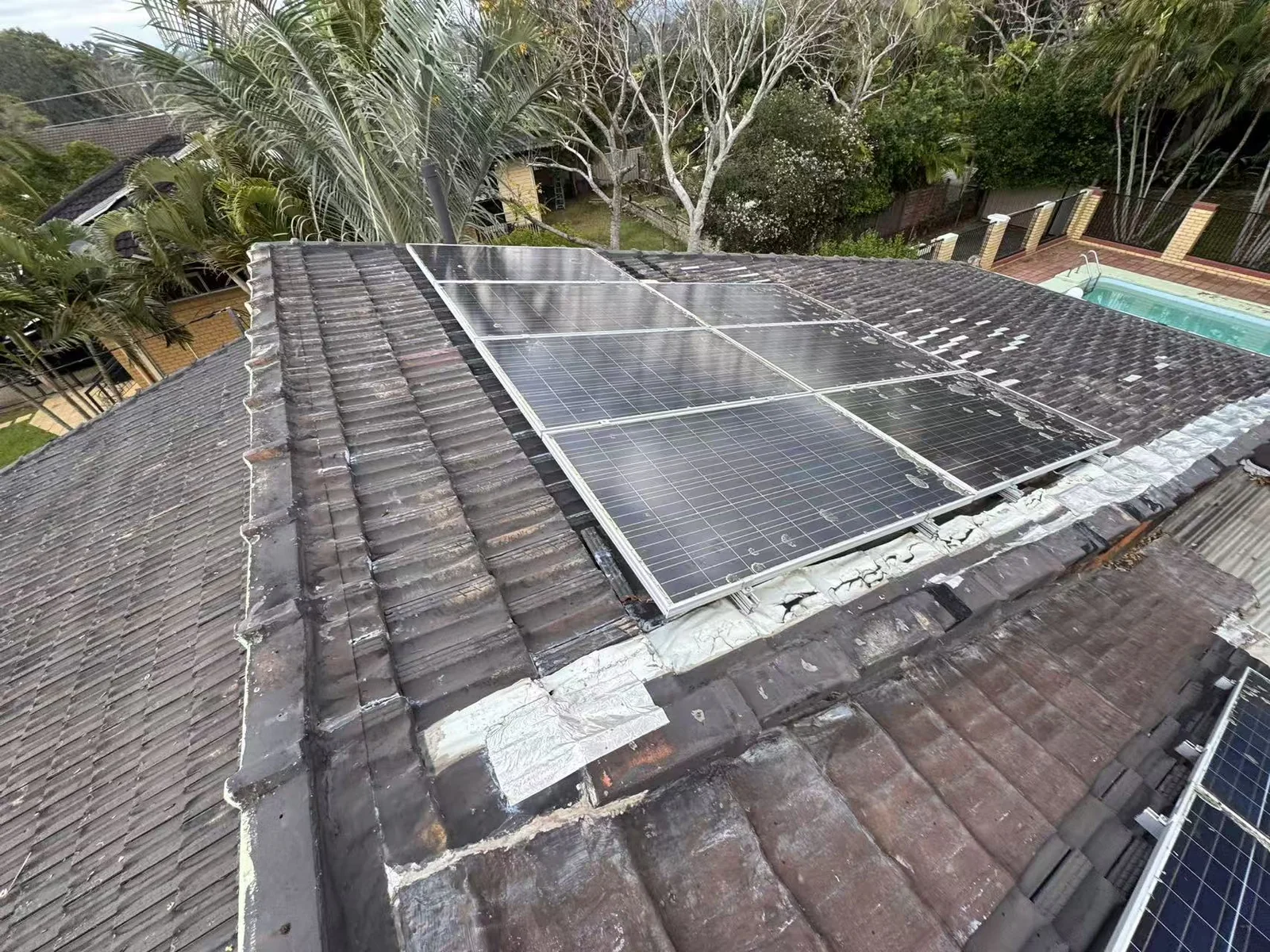 Wide roof-level view showing weathered concrete tiles and untidy patching around an existing solar panel array